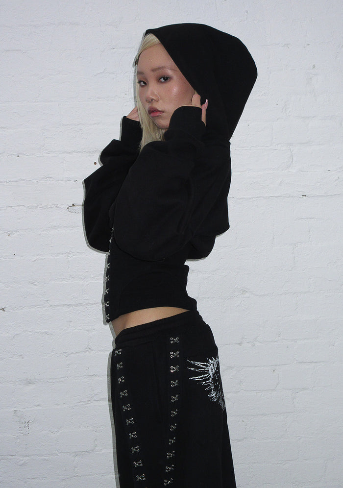 Model wearing black fallen corset sculpt hoodie with corset waist detailing in a side view.