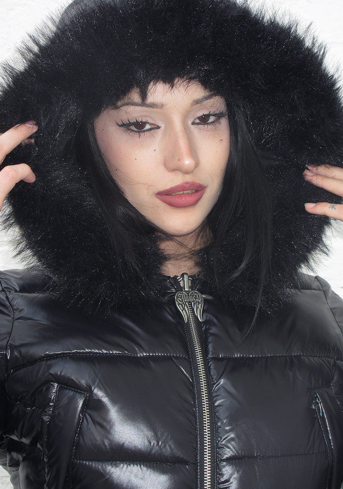 Close-up of a model wearing a black puffer jacket with a faux fur hood and a zip closure.