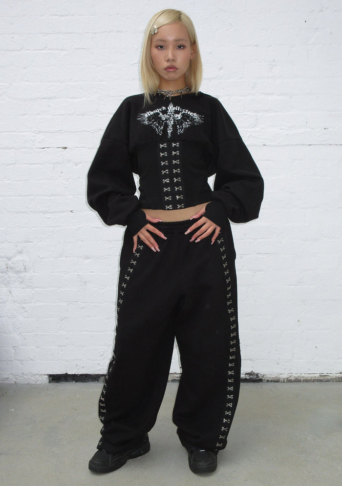 Model wearing black fallen hook and eye oversized sweatpants with hook-and-eye detailing on the sides.