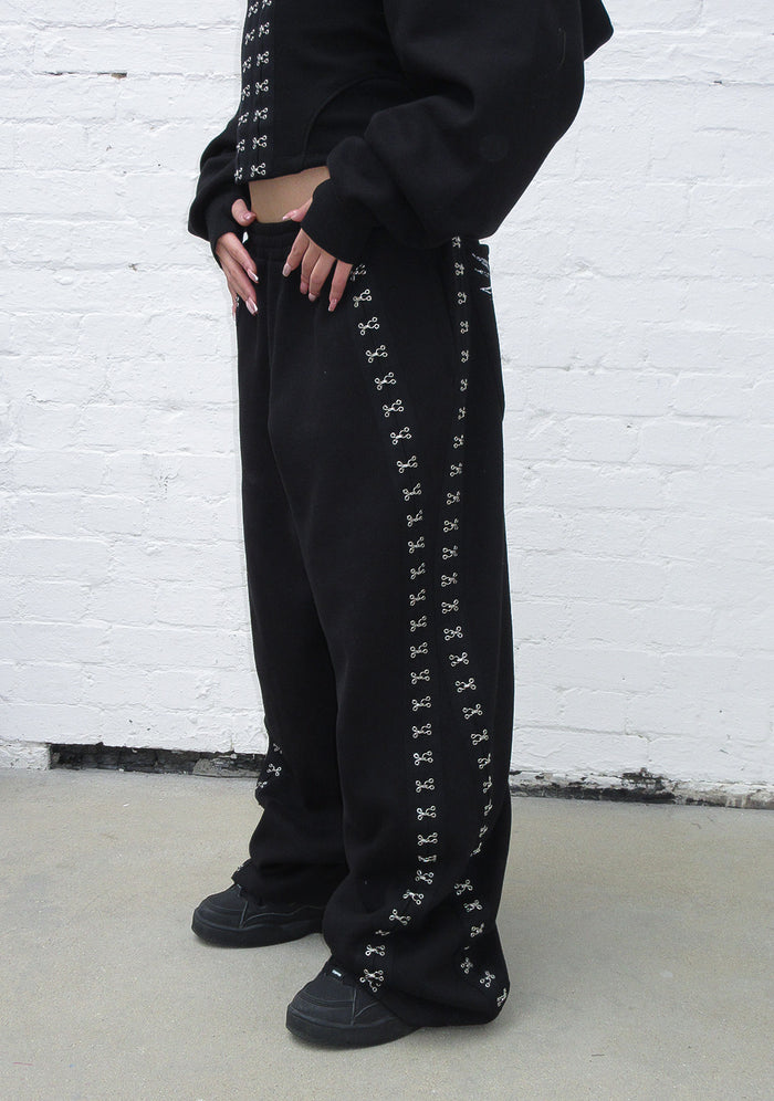 Model wearing black oversized sweatpants featuring hook-and-eye detailing on the sides.