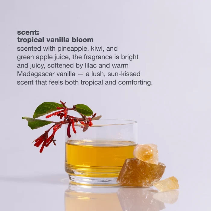 Glass of yellow liquid with a tropical vanilla bloom branch and ginger root on a light gray background