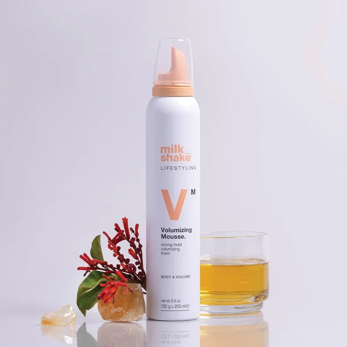 Milk Shake Volumizing Mousse bottle with a glass of liquid on a light gray background