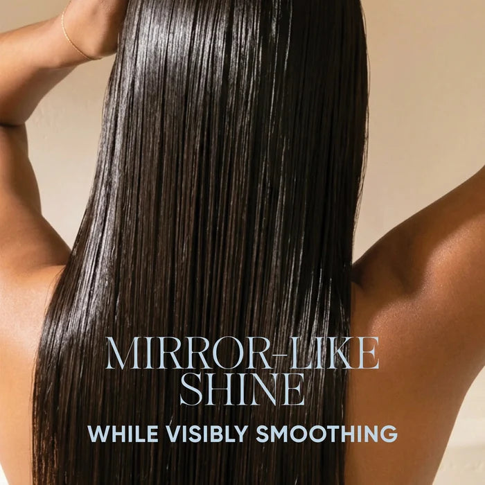 A person shown from the back with long, straight, glossy dark hair and arms raised, holding a comb near the scalp. Text at the top reads 'SIGNATURE SENSES POWERED BY BIOTECH ACTIVES' and the lower text reads 'MIRROR-LIKE SHINE WHILE VISIBLY SMOOTHING.