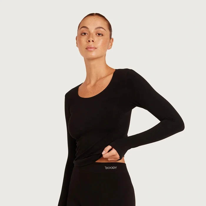 A woman modeling a black long-sleeve scoop-neck athletic top and matching black leggings against a light gray studio background. The brand name 'BOODY' is visible on the waistband of the leggings.